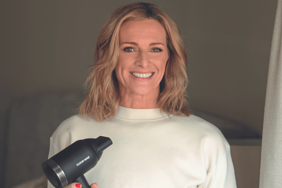 Gabby Logan holding a hairdryer and smiling