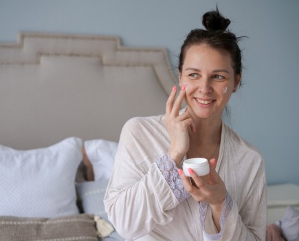 woman using face cream in bed, evening skincare routine