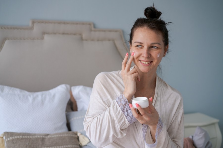 woman using face cream in bed, evening skincare routine